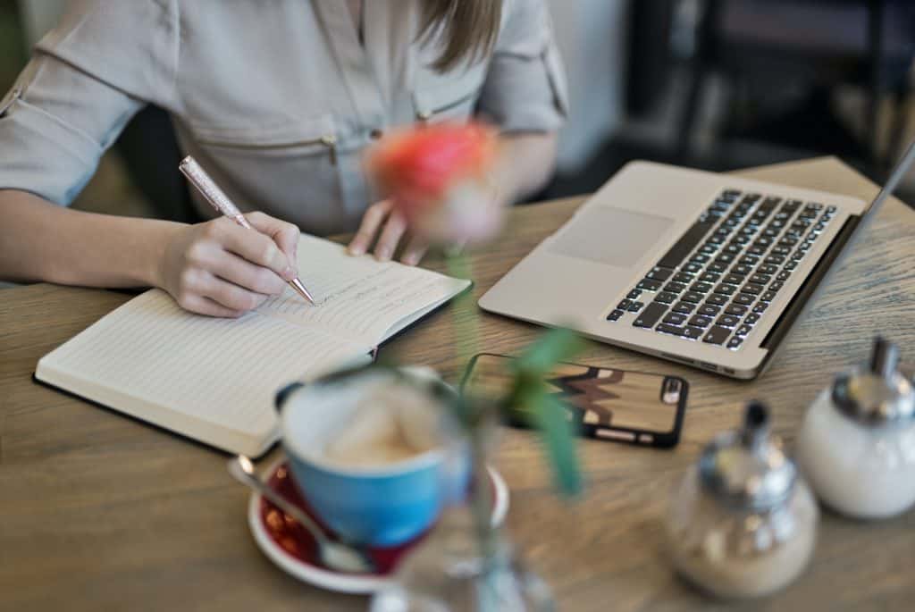 Person Writing On A Notebook Beside Macbook 1766604